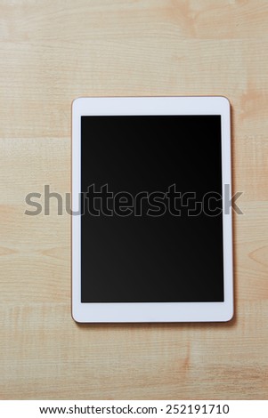 White digital tablet on a wooden desk with blank screen, space for text, top view