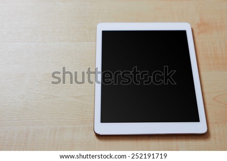 Front view of a white digital tablet on a wooden desk with blank screen, space for text