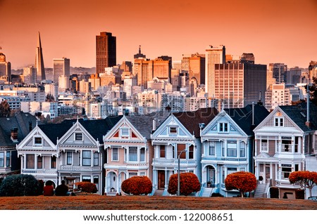 Row of colourful Victorian homes on Steiner Street with the San Francisco skyline behind.