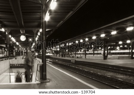 Black and White shot of an empty train station at night with a few people blurred and walking