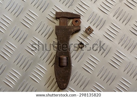 Adjust to Fit.\
An old rusty adjustable spanner or wrench holding a nut with two different sized and shaped nuts alongside.
