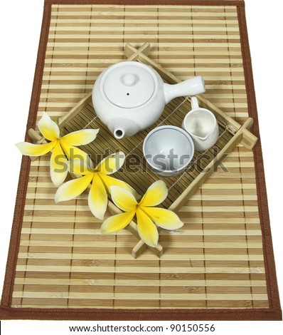 A set of tea (teapot, cup, milk jug) made from porcelain with yellow frangipani flower on bamboo mat