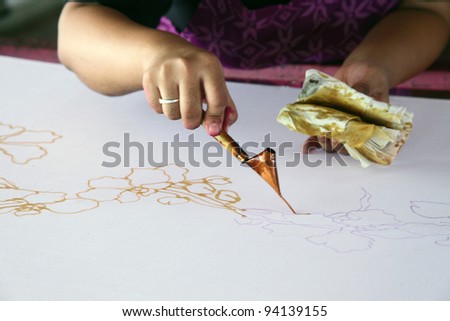 An artist carefully trace the floral motif on a traditional batik fabric using melted wax