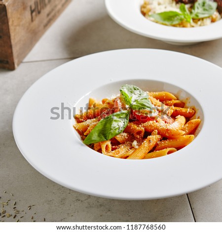 Tomato Penne Pasta Al Dente with Tomato Sauce, Parmigiano Reggiano Cheese, Cherry Tomatoes and Basil in White Plate Close Up. Traditional Italian Macaroni in Restaurant