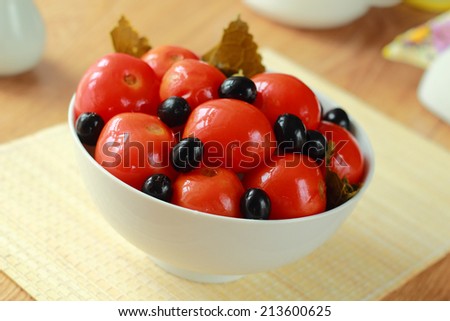 Canned tomatoes of red color with olives in a dish on a table
