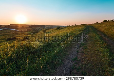 Field with country road and beautiful sunset