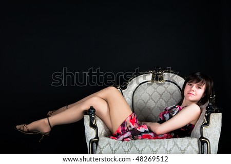 portrait of a beautiful girl sitting in white armchair on a black background