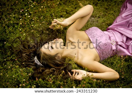 Beautiful princess lying in a the grass, about to kiss her frog prince