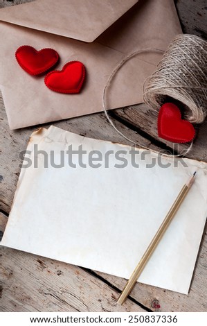 Old white sheet of paper and a pencil on a wooden background.The envelope,coil of twine and  little red hearts.