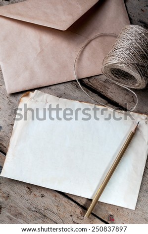 Old white sheet of paper and a pencil on a wooden background.The envelope and the coil of twine.