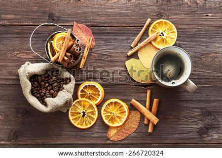 Dry orange and lemon, coffee beans in the bag, cinnamon, a Cup of hot coffee and fallen autumn leaves on wooden brown background.