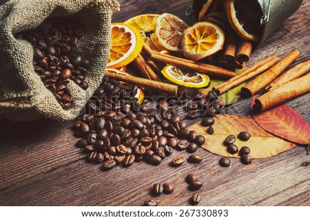 Dry lemon and orange, coffee beans in the bag, cinnamon and fallen autumn leaves on wooden brown background.