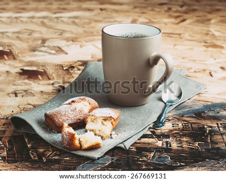 A Cup of coffee ,sugars and metal spoon, biscuits sprinkled with sugar on a napkin on a wooden table.