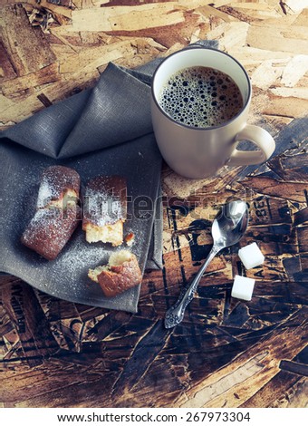 A Cup of coffee ,sugars and metal spoon, biscuits sprinkled with sugar on a napkin on a wooden table.