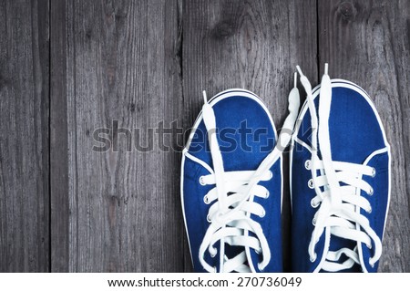 Youth blue sneakers with white untied the laces on wooden background