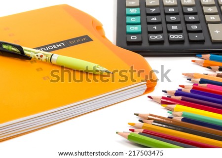 Pen lying on the diary next to a calculator and a set of colored pencils isolated on white background