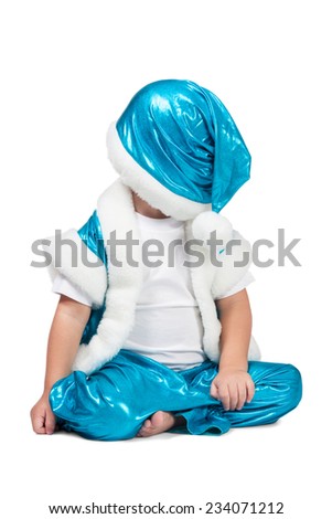 Kid in blue suit of Santa sitting on the floor and put his hat over his eyes isolated on white background