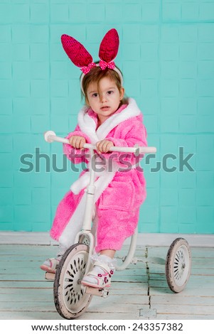 Little cute girl in pink rabbit costume sits on an old tricycle
