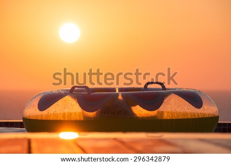 Transparent Inflatable Swim Ring on a Swimming Pool Deck overlooking the Sea with Sun Setting