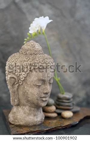 Stone Buddha head sculpture, stones, and flower in watery element.
