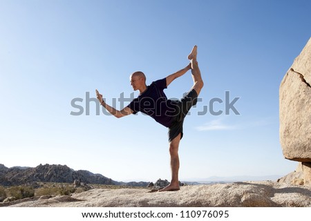 Man in the yoga pose Natarajasana outdoors balanced on a stone surface in the desert.