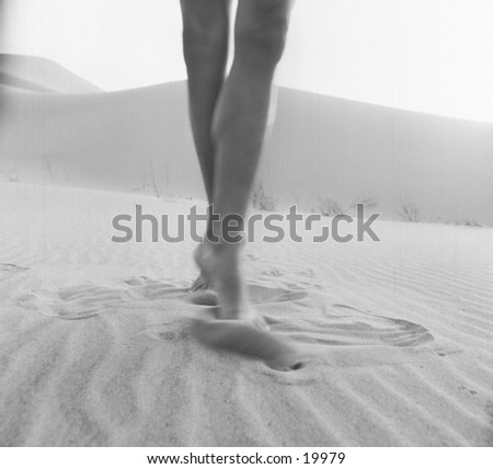 A woman's movement blurred long legs happily dance on a sand dune.