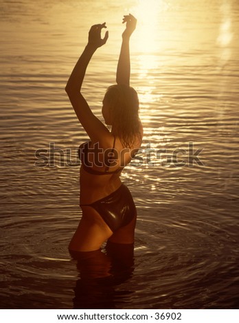 An inspired woman in a body of water raises her hands in the sun.