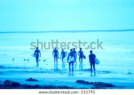 Soft focus motion blurred blue toned images of surfers. Large group of surfers walking down the beach.
