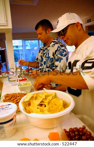 Two young adult men getting some food at the house party.