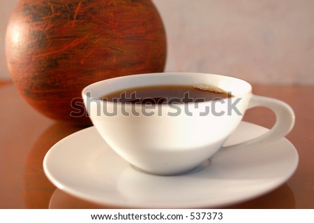 Coffee in a modernist white china cup next to an abstract orb. Extreme shallow depth of focus.