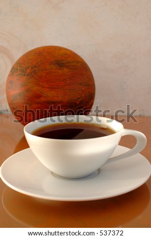 Coffee in a modernist white china cup next to an abstract orb. Extreme shallow depth of focus.