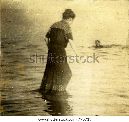 Vintage woman wading in towards submerged swimming man. Circa 1910. Photo very old with many scratches, fading, and solarizing qualities.