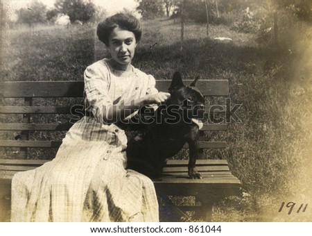 Vintage portrait of a young woman and her black dog sitting on a park bench.  Original Circa 1911 print has scratches, artifacts, fading and solarization qualities.