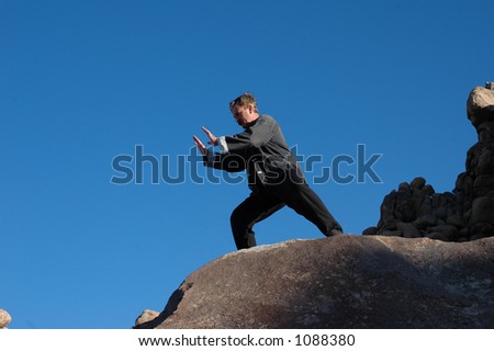 Deeply shadowed mid aged man practicing Tai Chi on giant rocks.