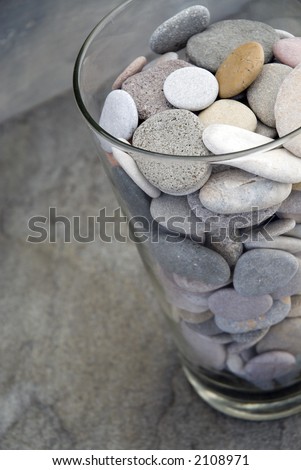 Mostly gray river stones in a glass vase sitting on gray slate.