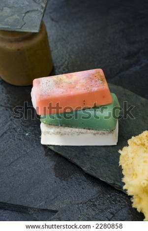 Organic soaps and sea sponge with earthen container on wet grey slate.