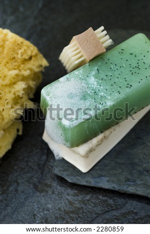 Organic soaps and sea sponge with small brush on wet grey slate.