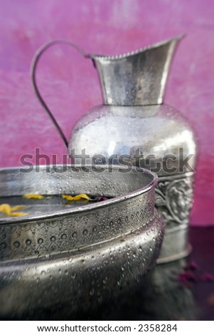 Ayurvedic Basin with yellow flower petals with Pitcher photographed next to a  pink wall. Soft image with shallow depth of focus.