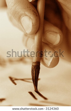 Chinese calligraphy. Close up of the rough fingers of an artist and brush. High ISO black and white sepia image.