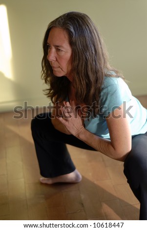 Middle aged female in a yoga pose: a deep squat with prayer hands.