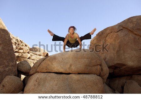 Free spirited man practicing hatha yoga posture titibasana on some giant rocks.