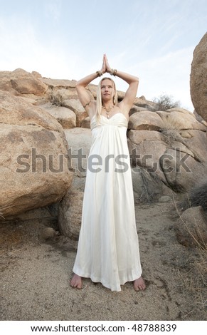 Young woman in white bridal gown in the desert with her hands in Temple Yoga Mudra.