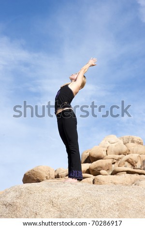 Woman in the yoga pose Urdhva Hastasana or standing with arms raised pose, in a natural rock landscape.