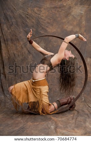 Studio photograph of a western tribal style woman wearing leather fringe dress and snakebone belt while moving in a large hoop.