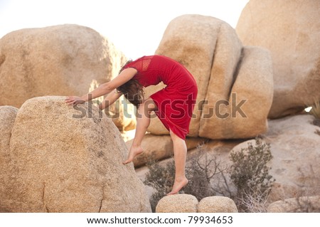 Woman in a red dress arched in a form mimicking giant stones.