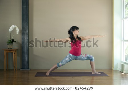 Woman in her forties practicing the powerful hatha yoga posture Virabrdrasana 2 or warrior 2. She is poised between light and dark, the duality which yoga seeks to unite.