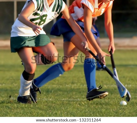 Two women battle for control of ball during field hockey game