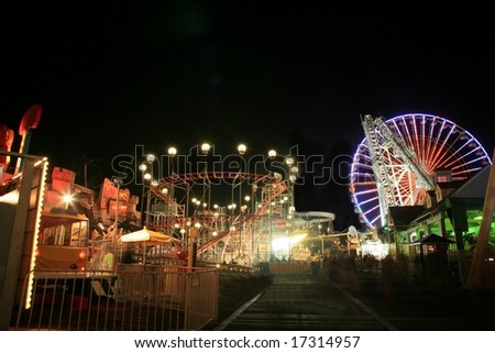 Blurry / long exposure image of a brightly lit amusement park rides on boardwalk