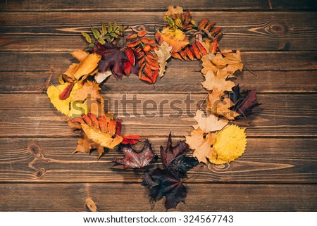 Background texture with old wooden table and yellow autumnal leaves folded in the shape of a heart