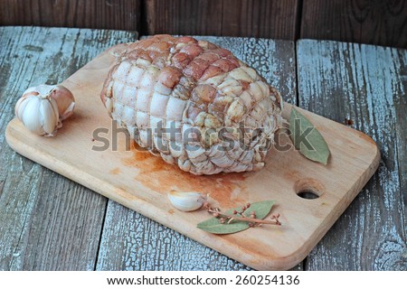 Raw chicken roll ready to roast on a cutting board with garlic and bay leaves